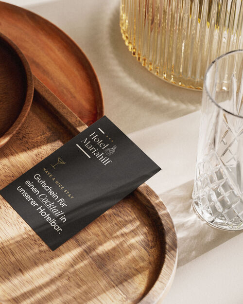 das Bild zeigt schwarzern Gutschein auf Holztabltett mit Kristallgläsern.